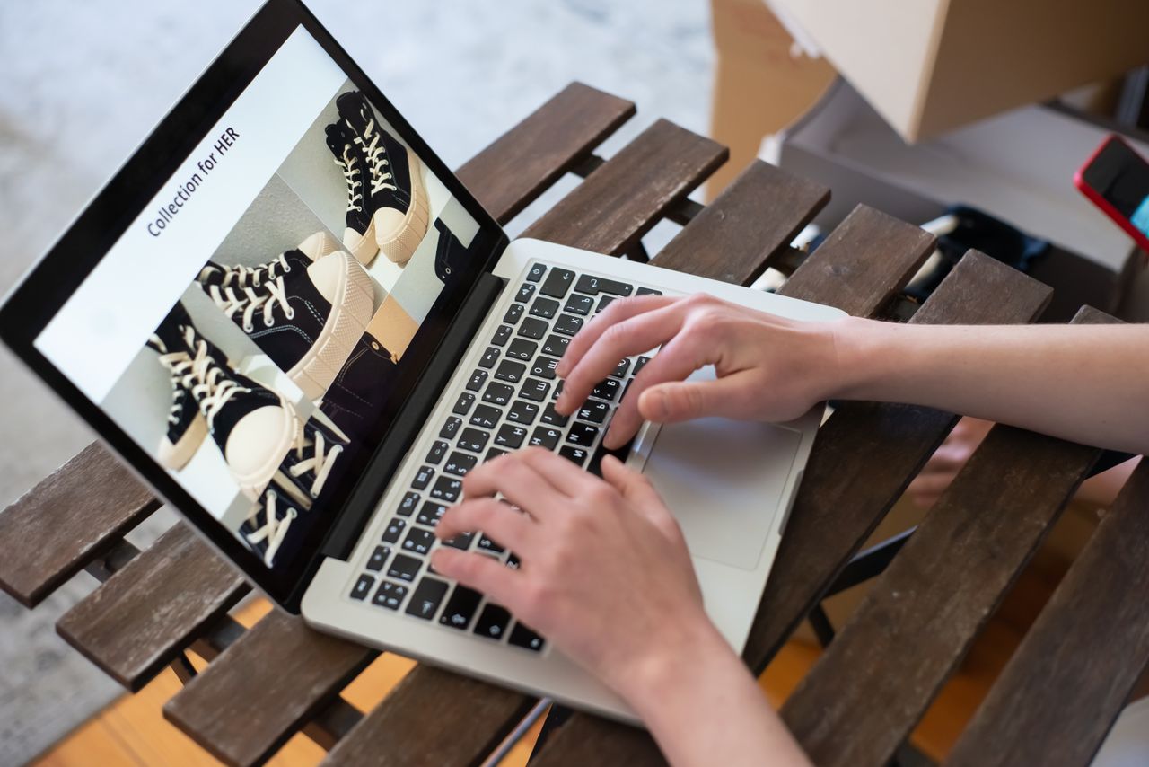 Des mains parcourant la Collection for HER sur une boutique de chaussures en ligne depuis un ordinateur portable.